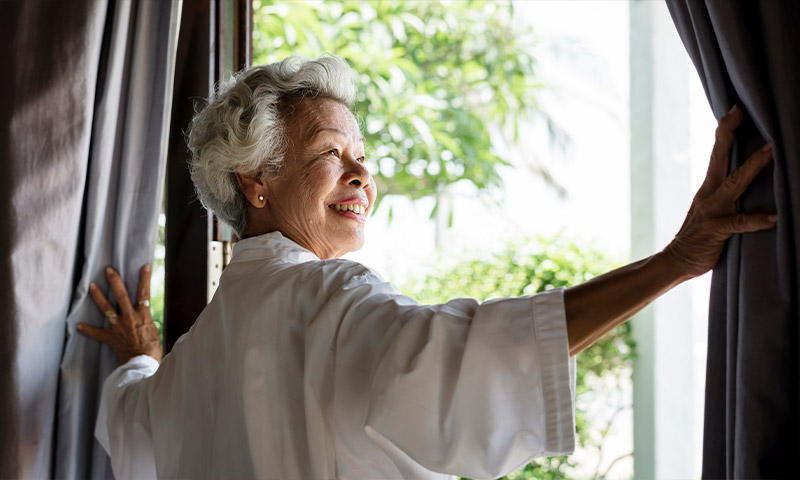 happy senior woman opening blinds financial planning